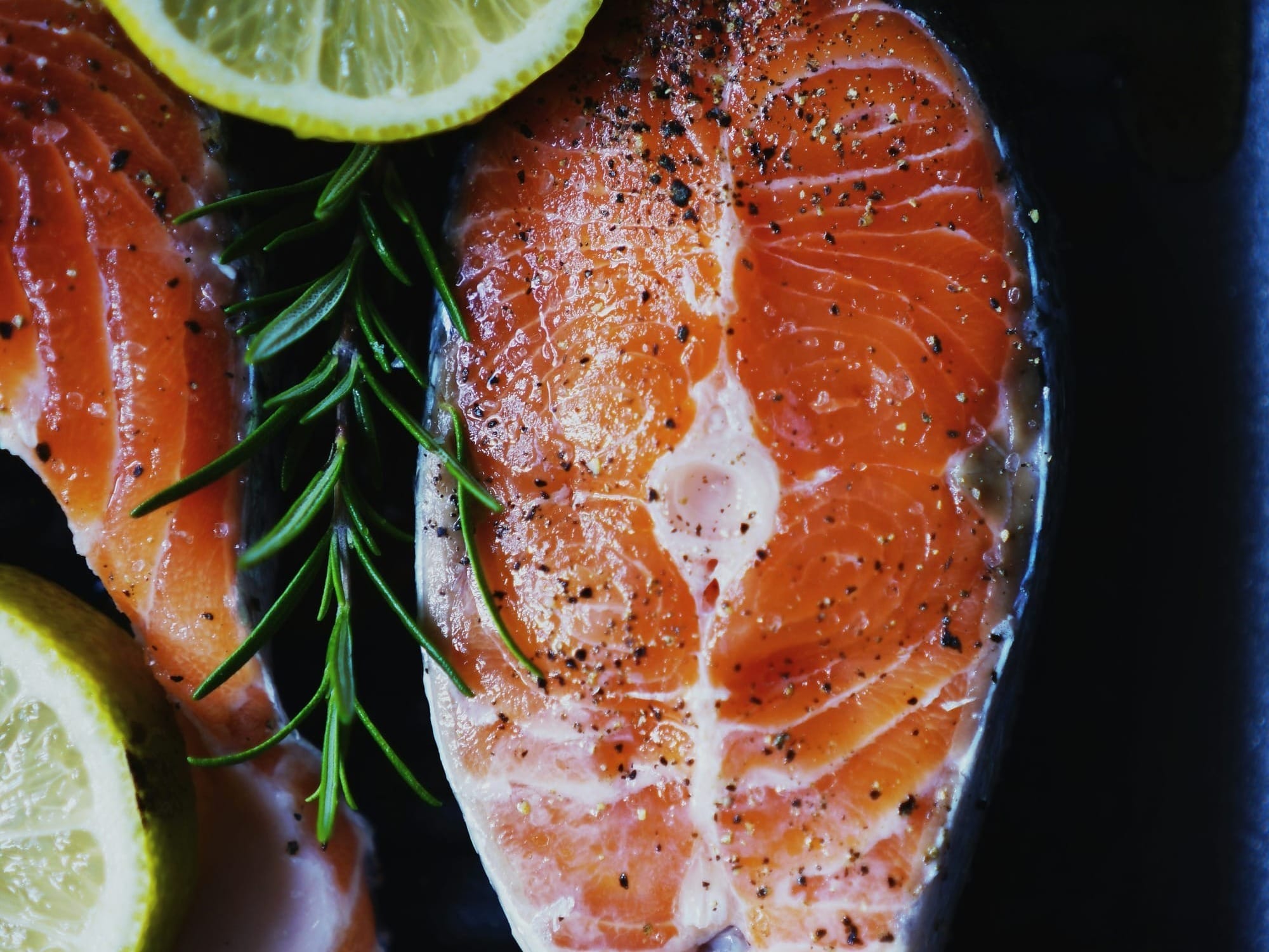 Fresh salmon steak garnished with rosemary, citrus and seasoned with pepper